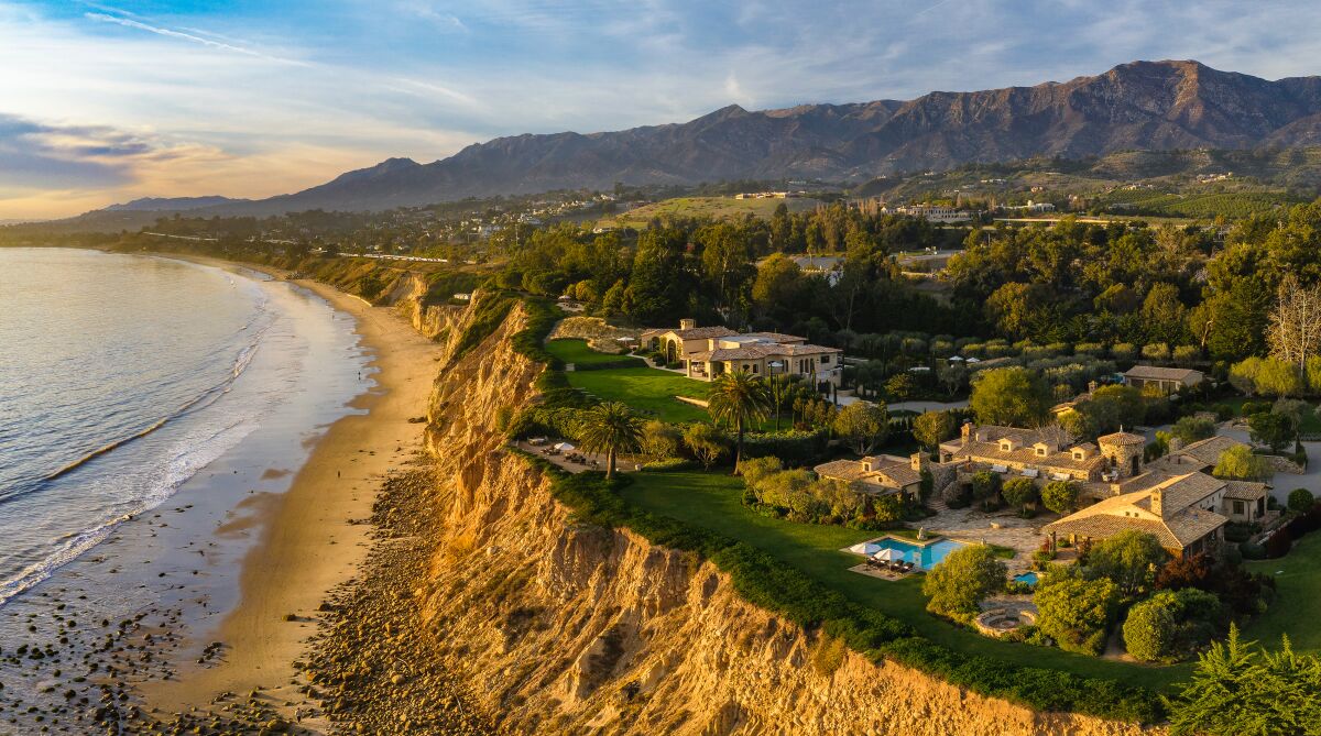 Homes with green lawns and one with a swimming pool are near a cliff.