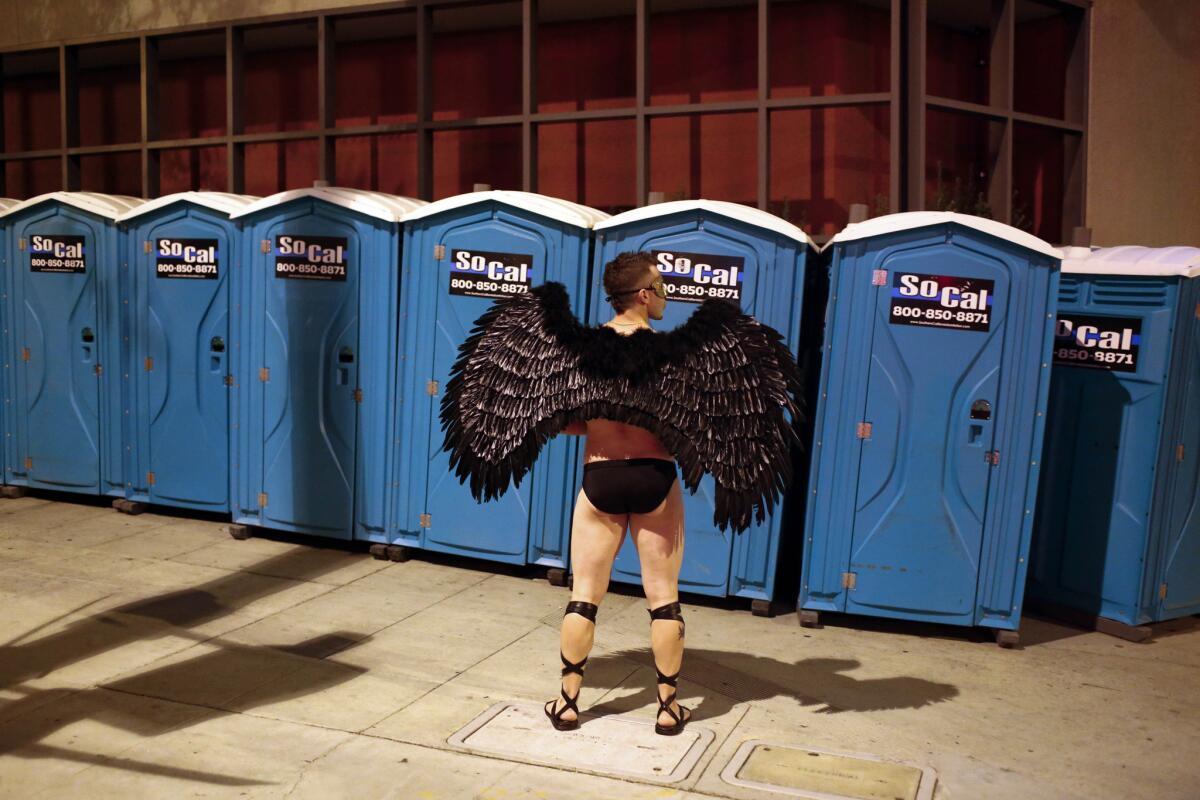 A man wearing wings waits at a row of portable toilets set up along Santa Monica Boulevard during the 2014 West Hollywood Halloween Carnaval.