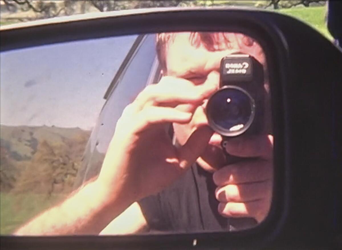 A reflection in a mirror of a man looking through a camera in the documentary "Sam Now."