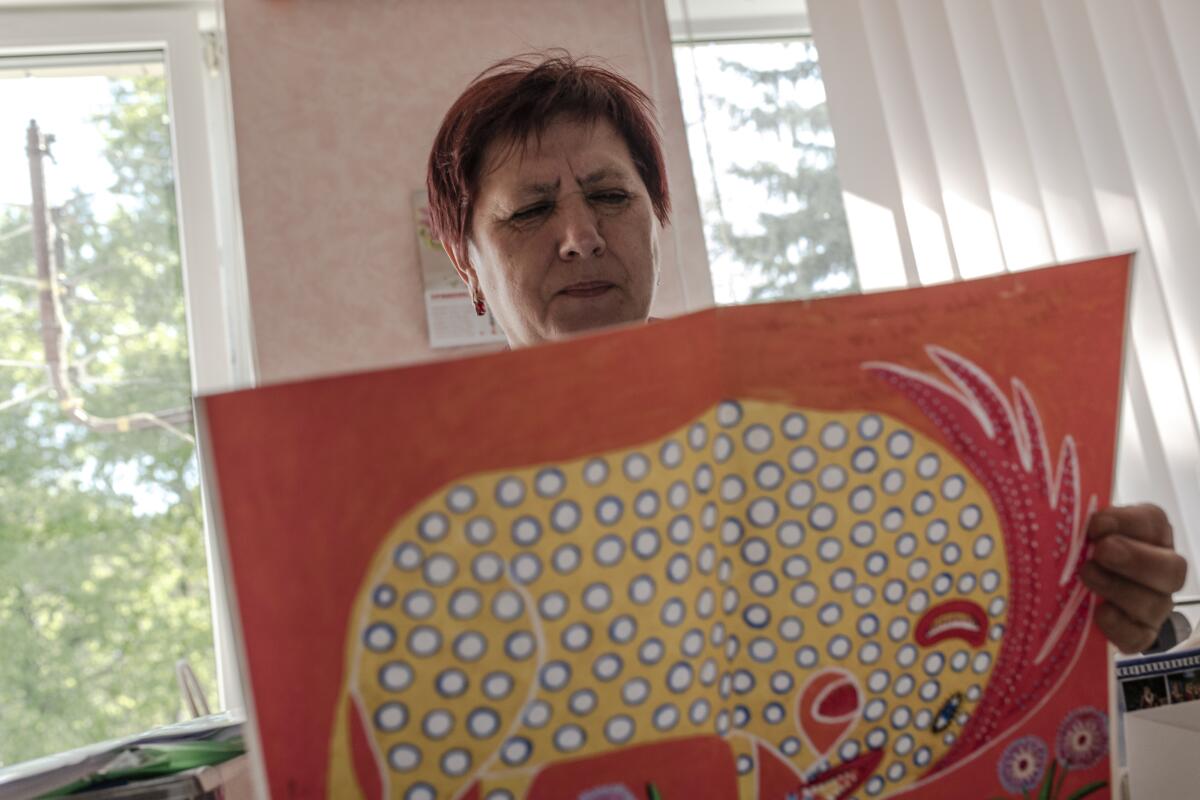 A woman holds a painting of a spotted animal with a horse-like mane.