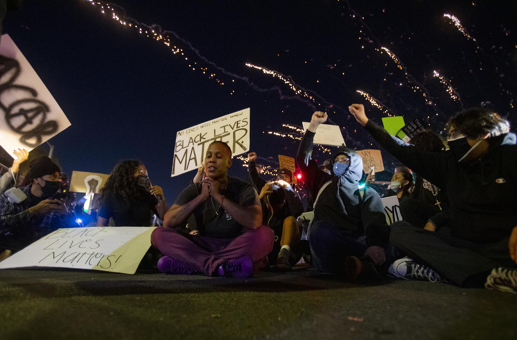 As fireworks explode in the background, Michelle Usher of Santa Ana, middle, prays in the street.
