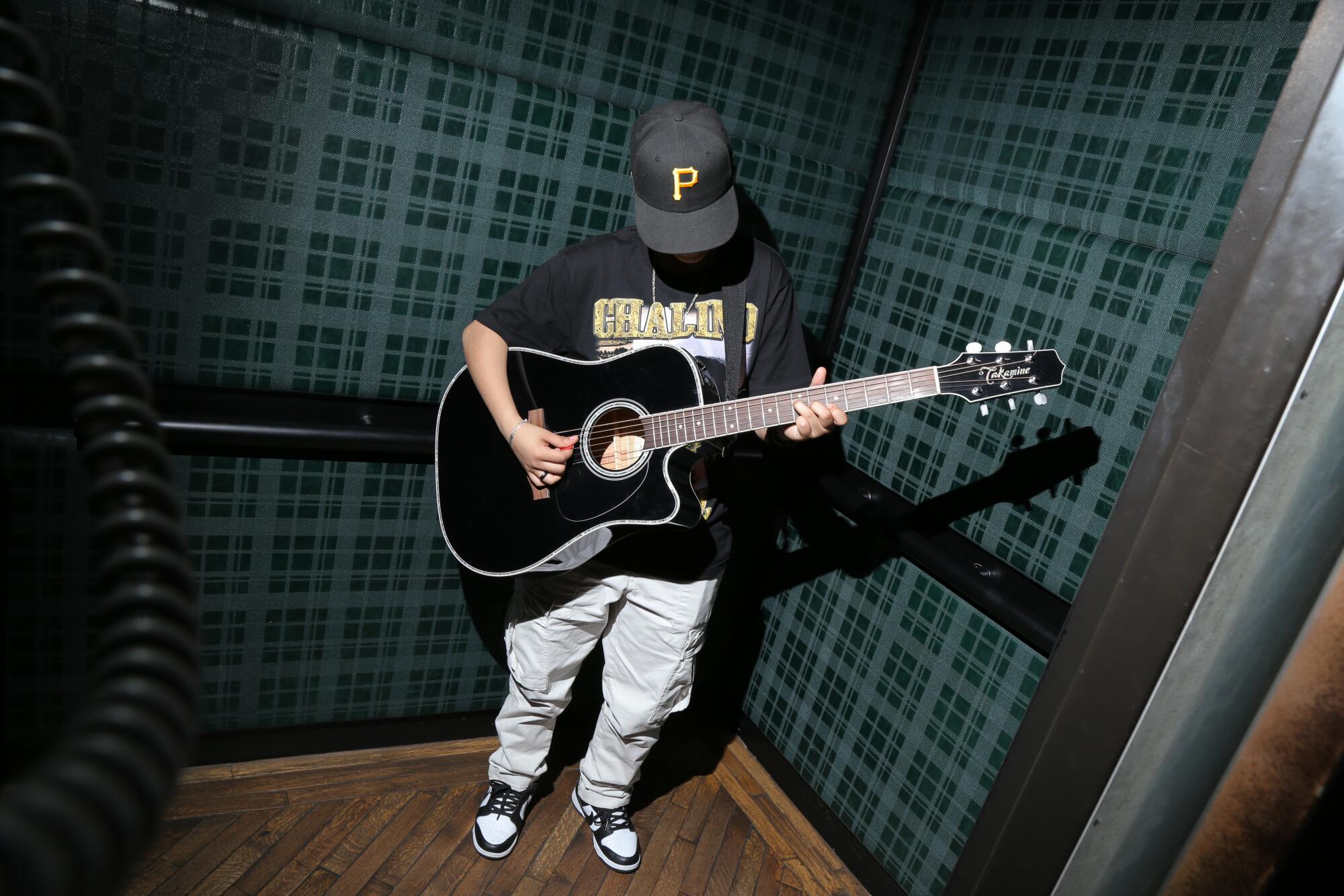 A person stands in a small elevator playing guitar.