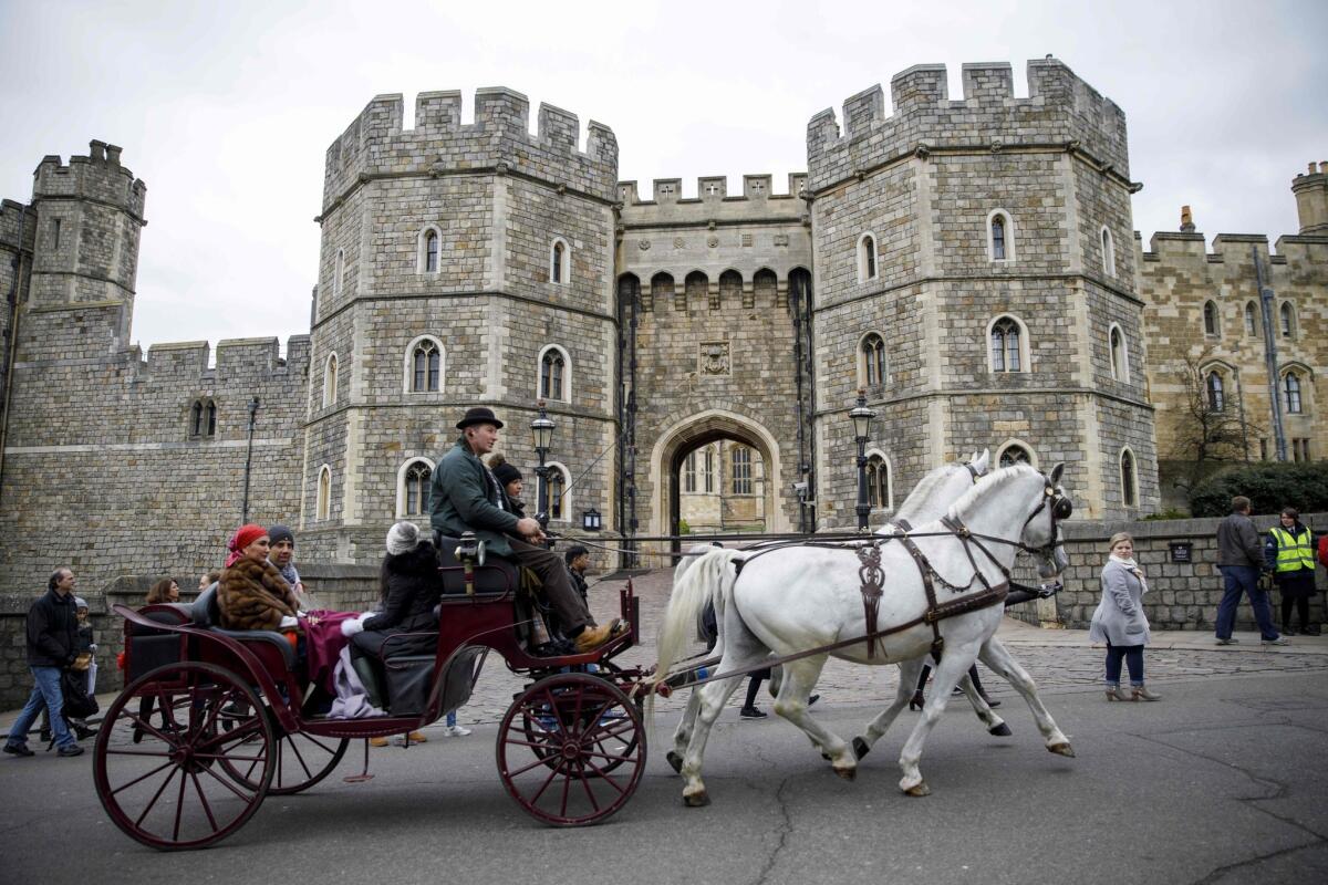 Tourists ride in a horse-drawn carriage past the main entrance of Windsor Castle.
