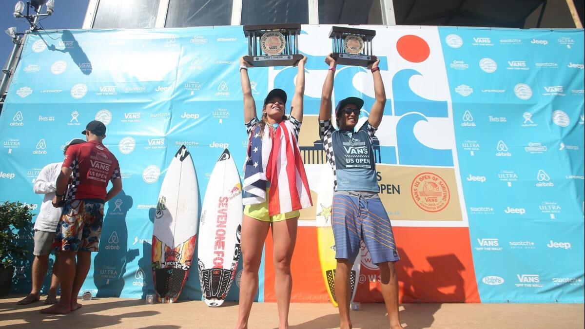 Locals Courtney Conlogue, left, and Kanoa Igarashi hold up their first-place trophies after they won the women's and men's U.S Open of Surfing titles in Huntington Beach on Sunday.