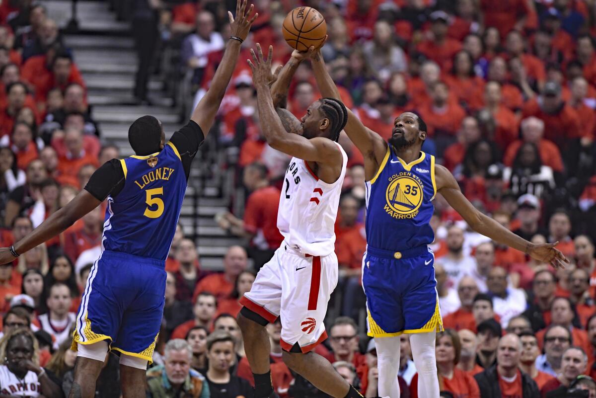 Kawhi Leonard, center, shoots under pressure from Golden State Warriors center Kevon Looney (5) and Kevin Durant.