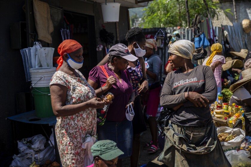 Customers wearing protective face masks as a precaution against the spread of the new coronavirus, talk with a vendor in a street market in Port-au-Prince, Haiti, Saturday, June 5, 2021. Haiti defied predictions and perplexed health officials by avoiding a COVID-19 crisis for more than a year, but the country of more than 11 million people that has not received a single vaccine is now battling a spike in cases and deaths. (AP Photo/Joseph Odelyn)