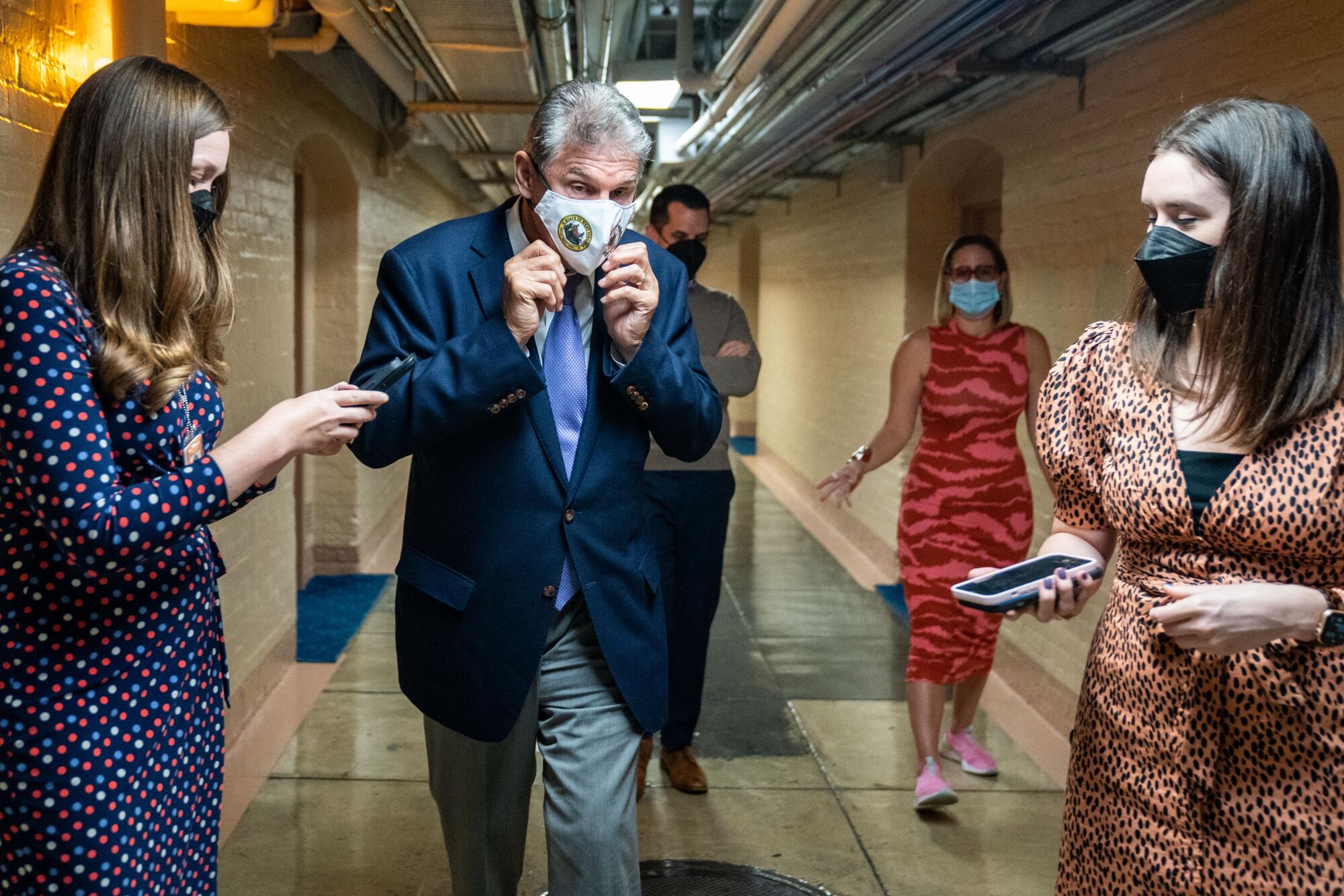 Sen. Joe Manchin adjusts his mask while talking to reporters