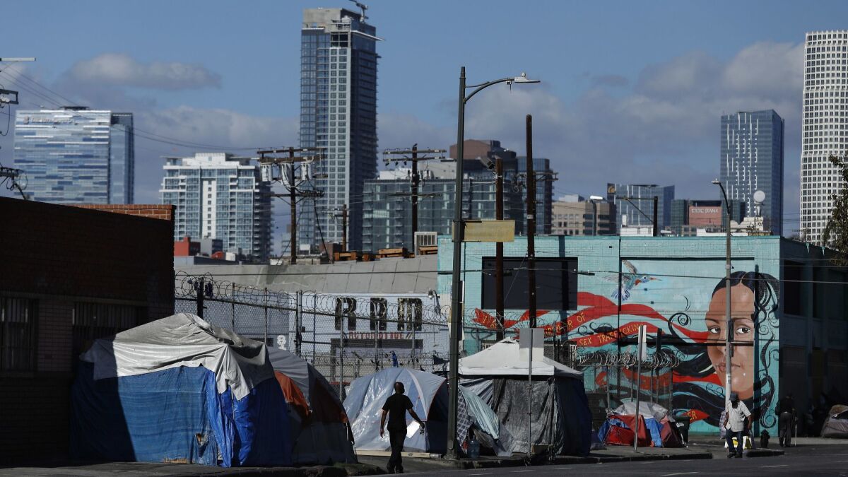 People walk past a homeless encampment on 6th St., just west of Central Ave. in downtown Los Angeles on Oct. 11.