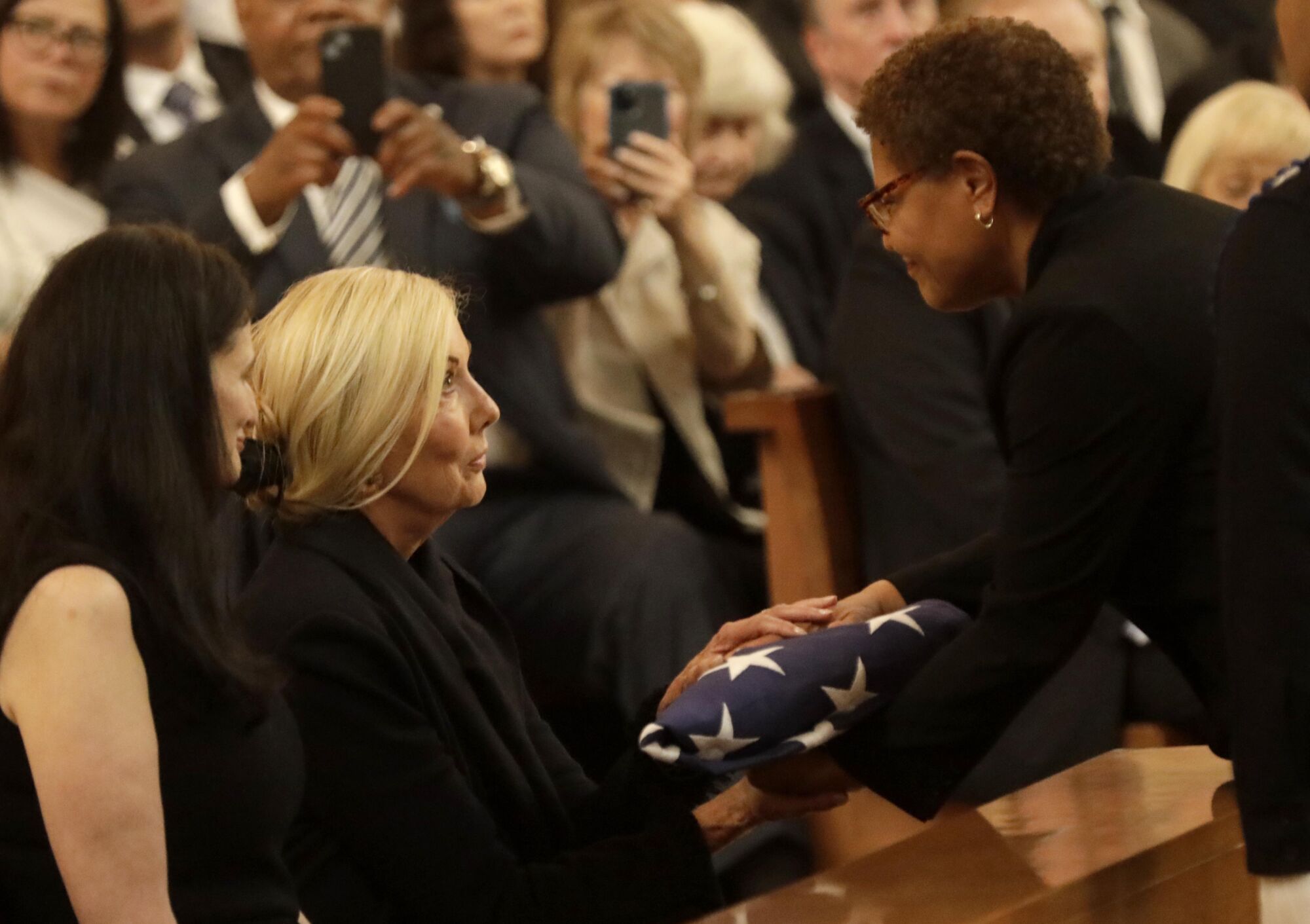 Los Angeles Mayor Karen Bass presents the U.S. flag to Elizabeth Riordan, the wife of the former Mayor Richard Riordan 