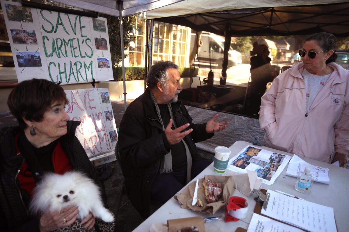 A man, woman and fluffy white dog sit at a booth at a farmer's market. 