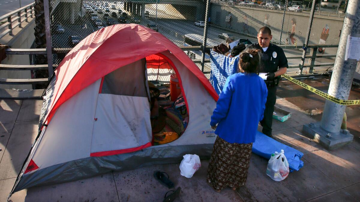 A police officer talks to a homeless woman outside of her tent on a freeway overpass in downtown Los Angeles.