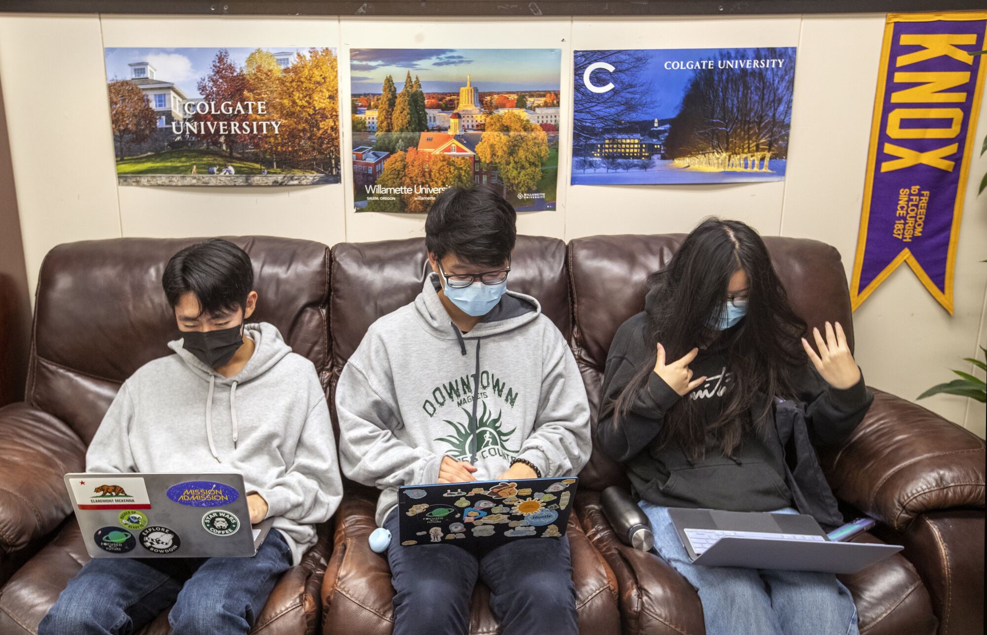Three students work on their college applications on laptops while sitting on a brown couch.