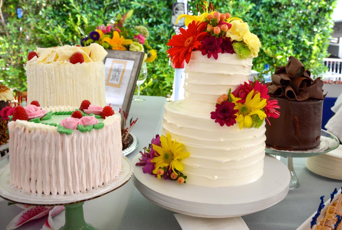 Several whole cakes decorated with flowers, fresh berries and chocolate curls, on a table in front of greenery