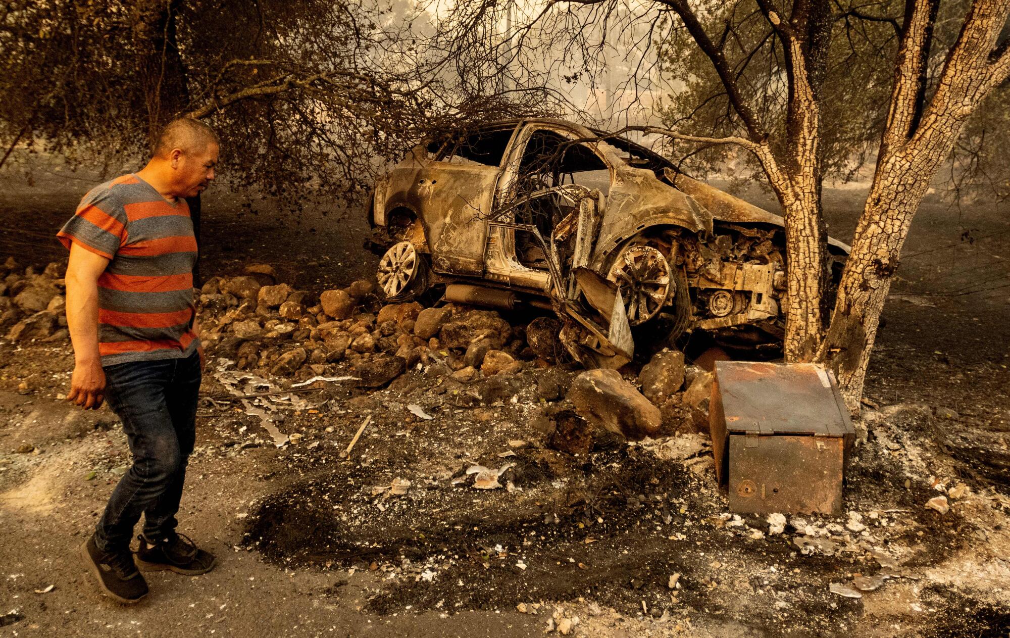 A man stands near a vehicle totally destroyed by fire.