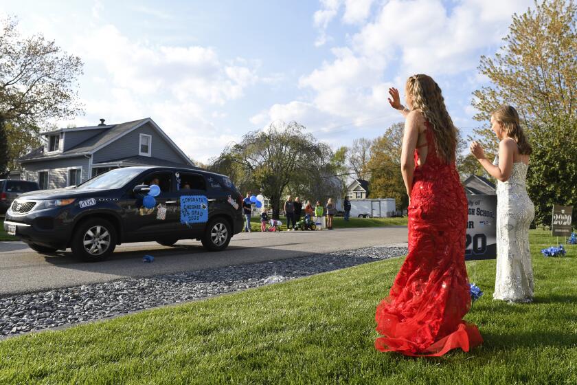 South River High School Class of 2020 seniors Chesnie Bell, second from right, and her best friend Meghan Wilborn, right, wear their prom dresses as they wave to family and friends driving by their home in Edgewater, Md., Monday, April 20, 2020. Because of the coronavirus pandemic, Bell's mother Trish Bell, arranged the "drive-by parade" to help lift her daughter's spirits. Many of the South River High School families found ways to celebrate their seniors given that prom, graduation and other traditional senior activities were canceled because of the coronavirus pandemic. (AP Photo/Susan Walsh)