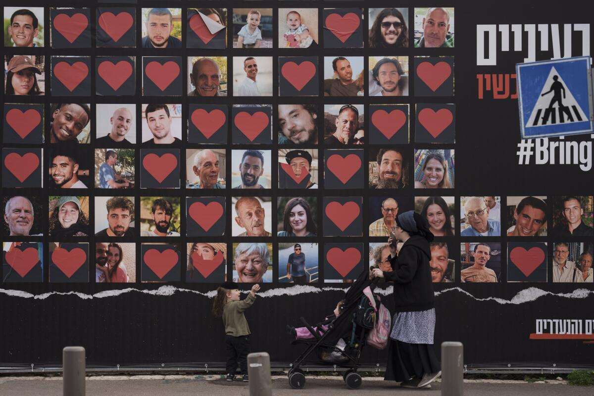 A woman and her children walk past a wall with photographs of Israeli hostages.
