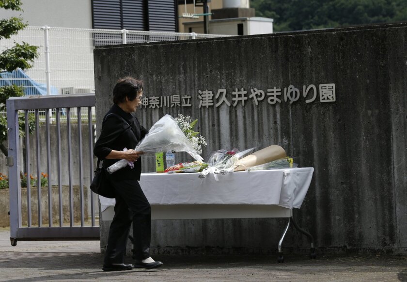 A woman offers a bouquet of flowers in front of the Tsukui Yamayuri-en, a facility for the mentally disabled where a number of people were killed and dozens injured in a knife attack in Sagamihara, outside of Tokyo, Wednesday, July 27, 2016. Japanese police on Wednesday searched the home of the suspect in the mass stabbing spree. (AP Photo/Shizuo Kambayashi)