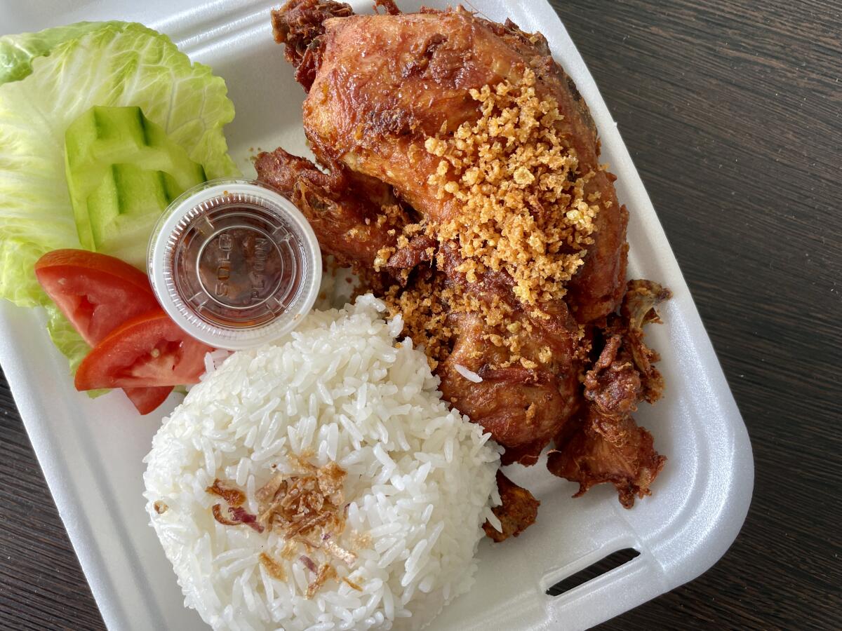 A styrofoam container of ayam kremes with penyet sambal, or fried chicken, with rice and garnishes.