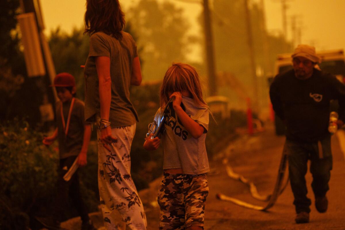 Gabi Frank runs with Jonah, 7, and Augie, 10, as workers hose down plants to protect a home on Pacific Coast Highway during the Woolsey fire in Malibu.