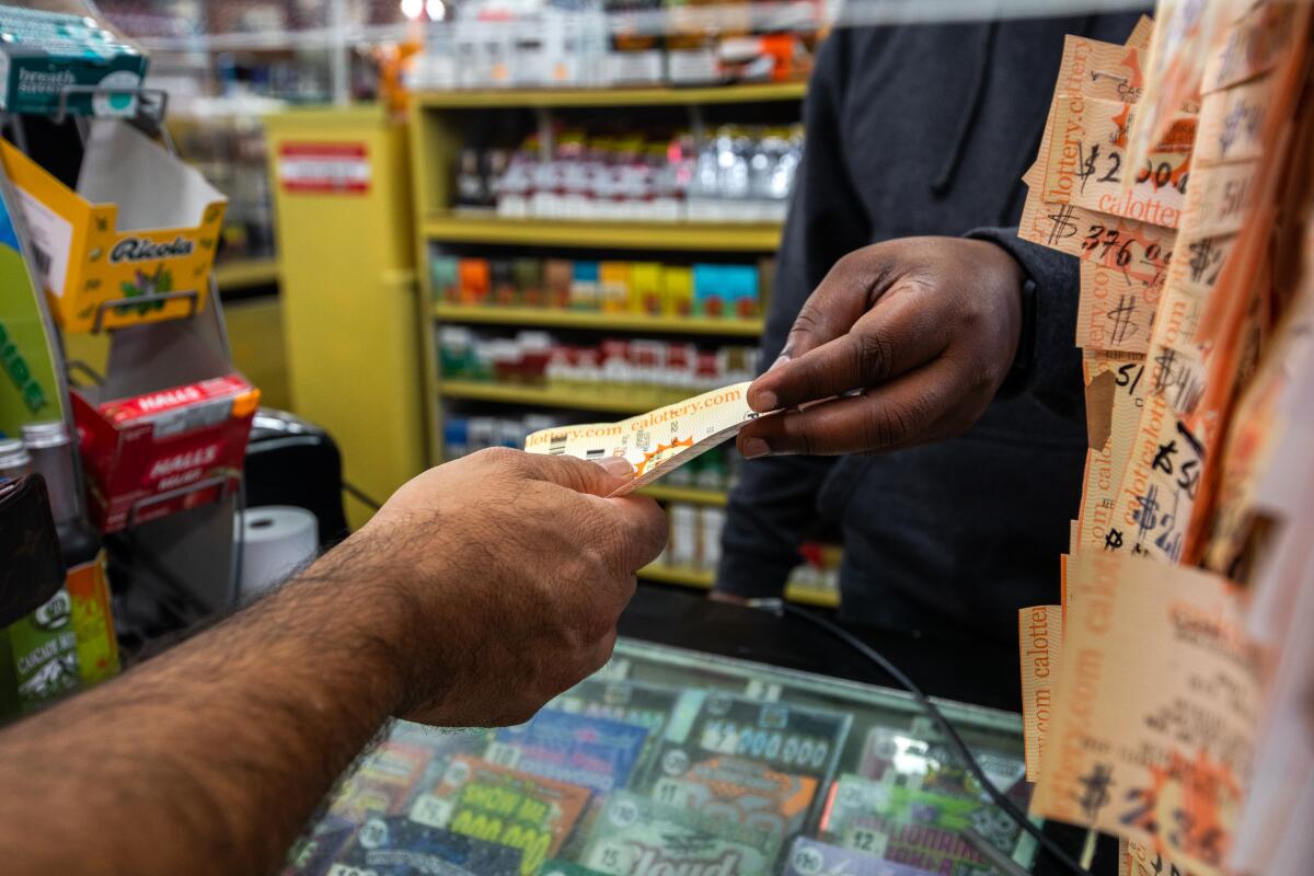 A close-up of a cashier handing a lottery ticket to a customer at a liquor store