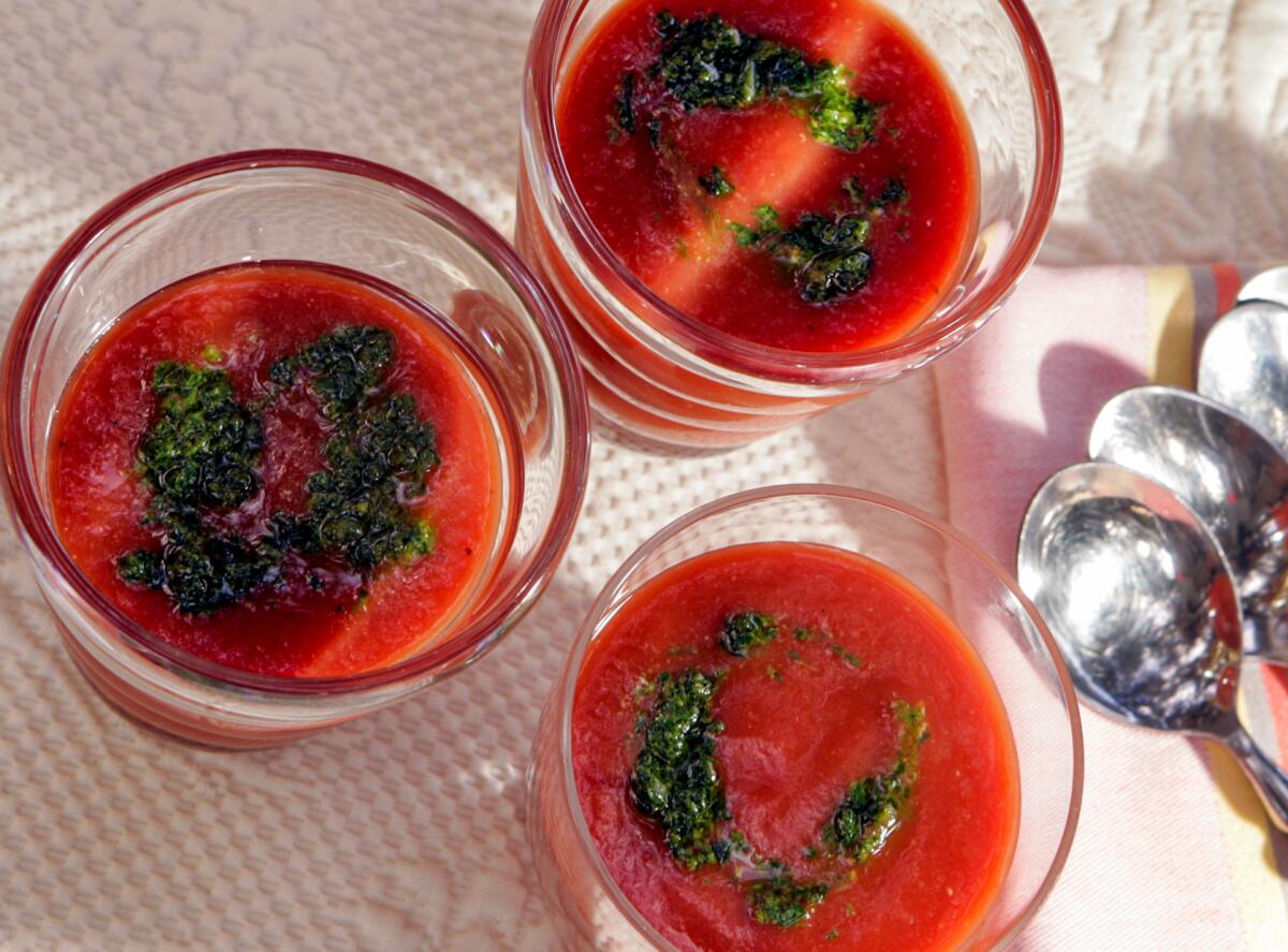Three glass cups filled with red soup with a squiggle of green topping