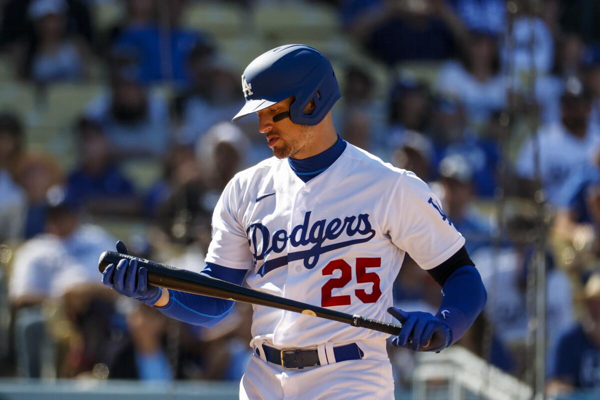 A man in a blue and white uniform with a blue batting helmet looks at a black bat during a game.