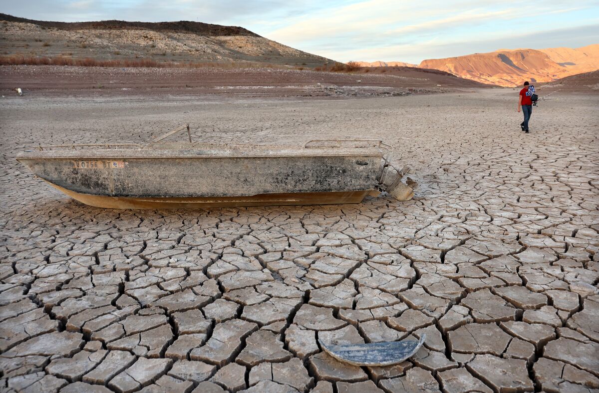 A person walks past a formerly sunken boat resting on a now-dry section of lakebed.