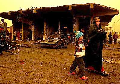 A woman and her son hurry by the scene where 15 were killed and 30 injured when two bombs of unknown origin struck a strip of workshops and apartments along a major highway running north of Baghdad on the the road to Mosul. A sandstorm darkened the daytime sky.