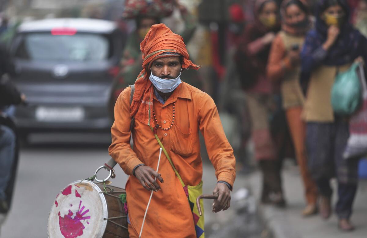 A man wears his face mask below his nose and walks in a market area with a traditional percussion instrument in Jammu, India, Saturday, Jan.15, 2022. It’s mandatory to wear a mask in India. And police are out on the streets, watching people to make sure they are in place. People caught without wearing a mask are fined. Some local governments, like the one in the capital New Delhi, have recruited new staff to ensure the rules are followed.c(AP Photo/Channi Anand)