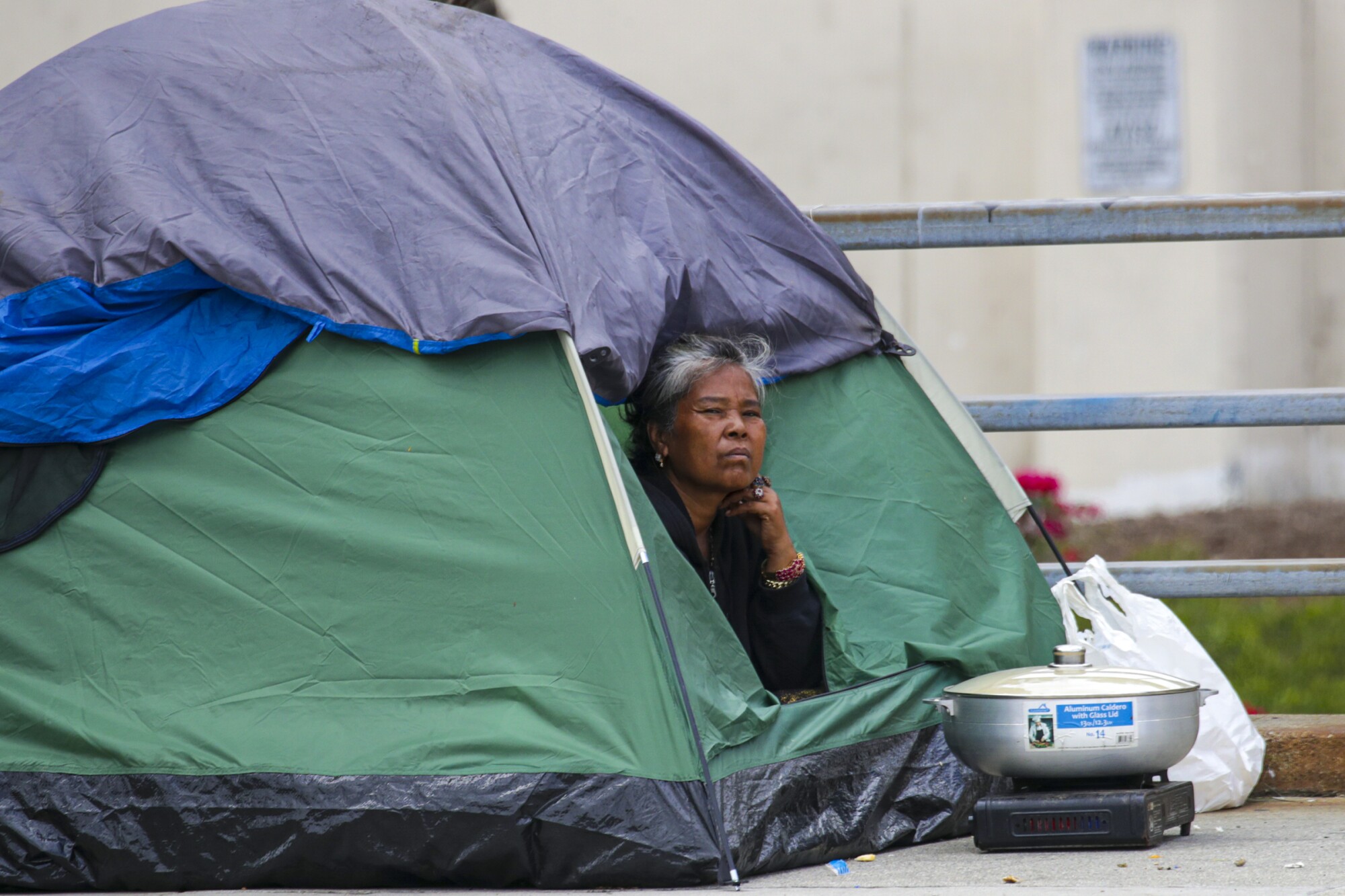 A homeless person peers out of her tent on Aliso Street in downtown Los Angeles on Friday.