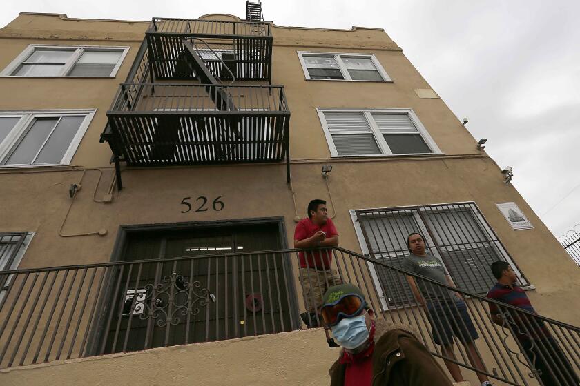 LOS ANGELES, CALIF. - APR. 18, 2020. Men stand outside an apartment building in the Westlake District of Los Angeles, which has the second highest population density in the city, with about 38,214 people per square mile. (Luis Sinco/Los Angeles Times)