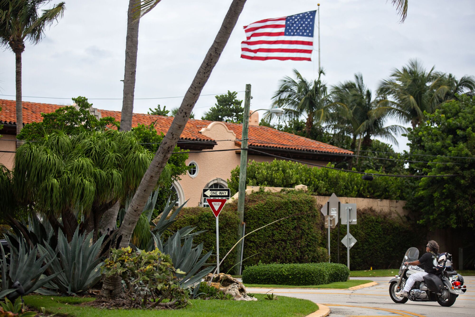 A large U.S. flag flies over Mar-a-Lago Club, seen from the street.