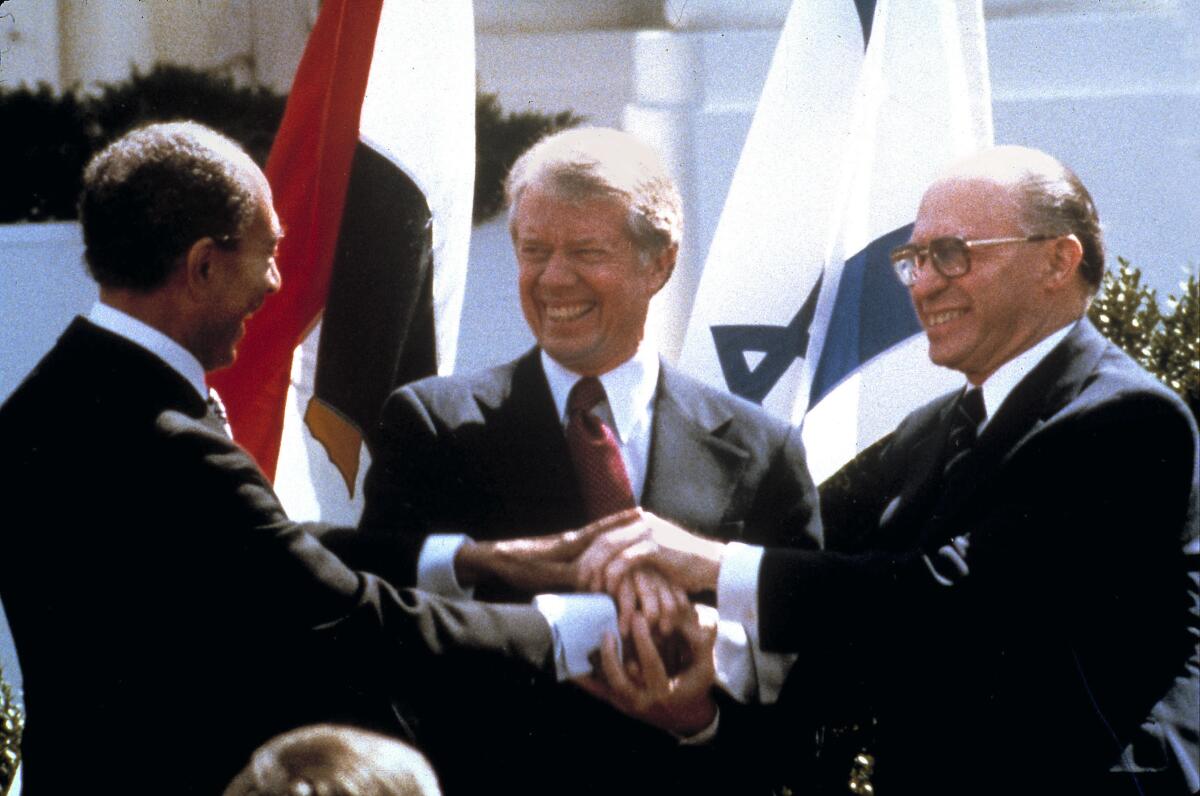 Three men smile and clasp hands.