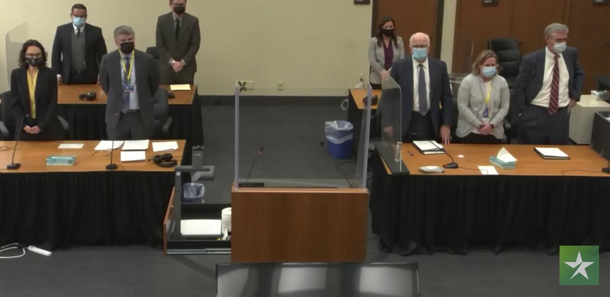 The prosecution team, left, and the defense, right, stand before tables in the courtroom. 