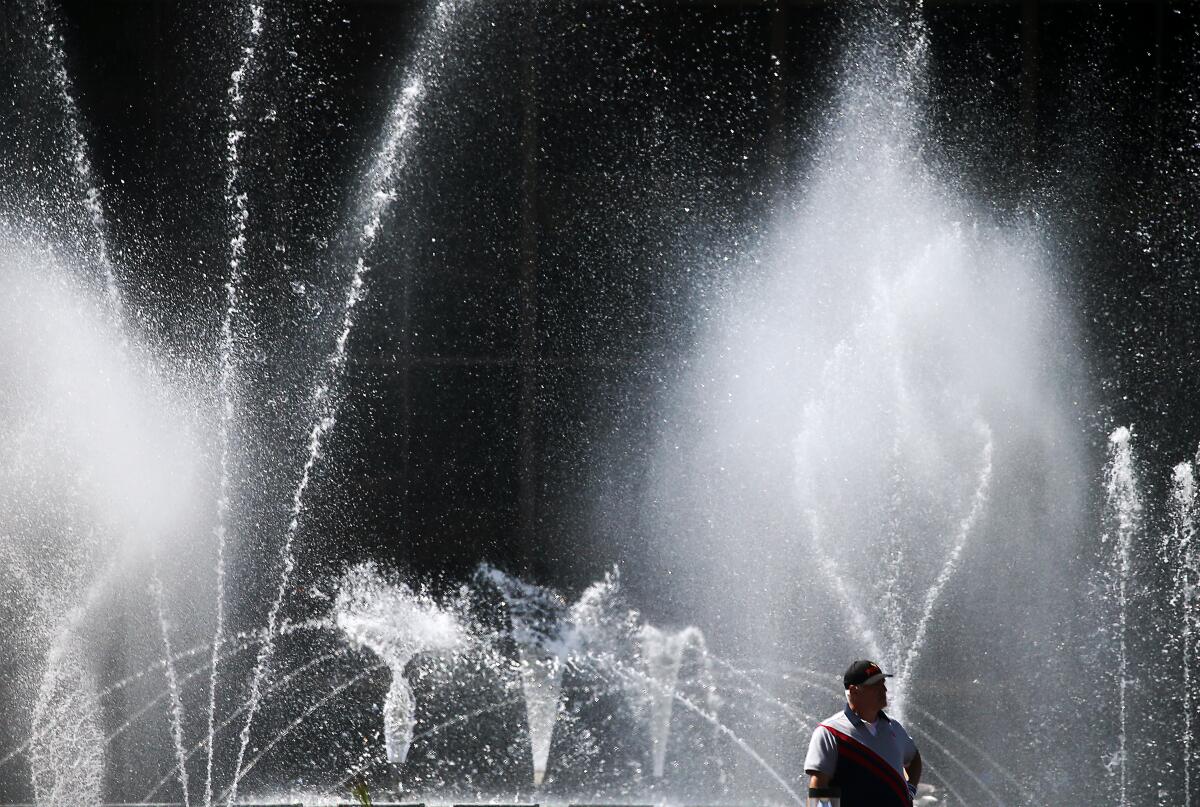 A man stands in the mist of fountains at the Long Beach Center Theater Plaza, where temperatures reached into the 80s