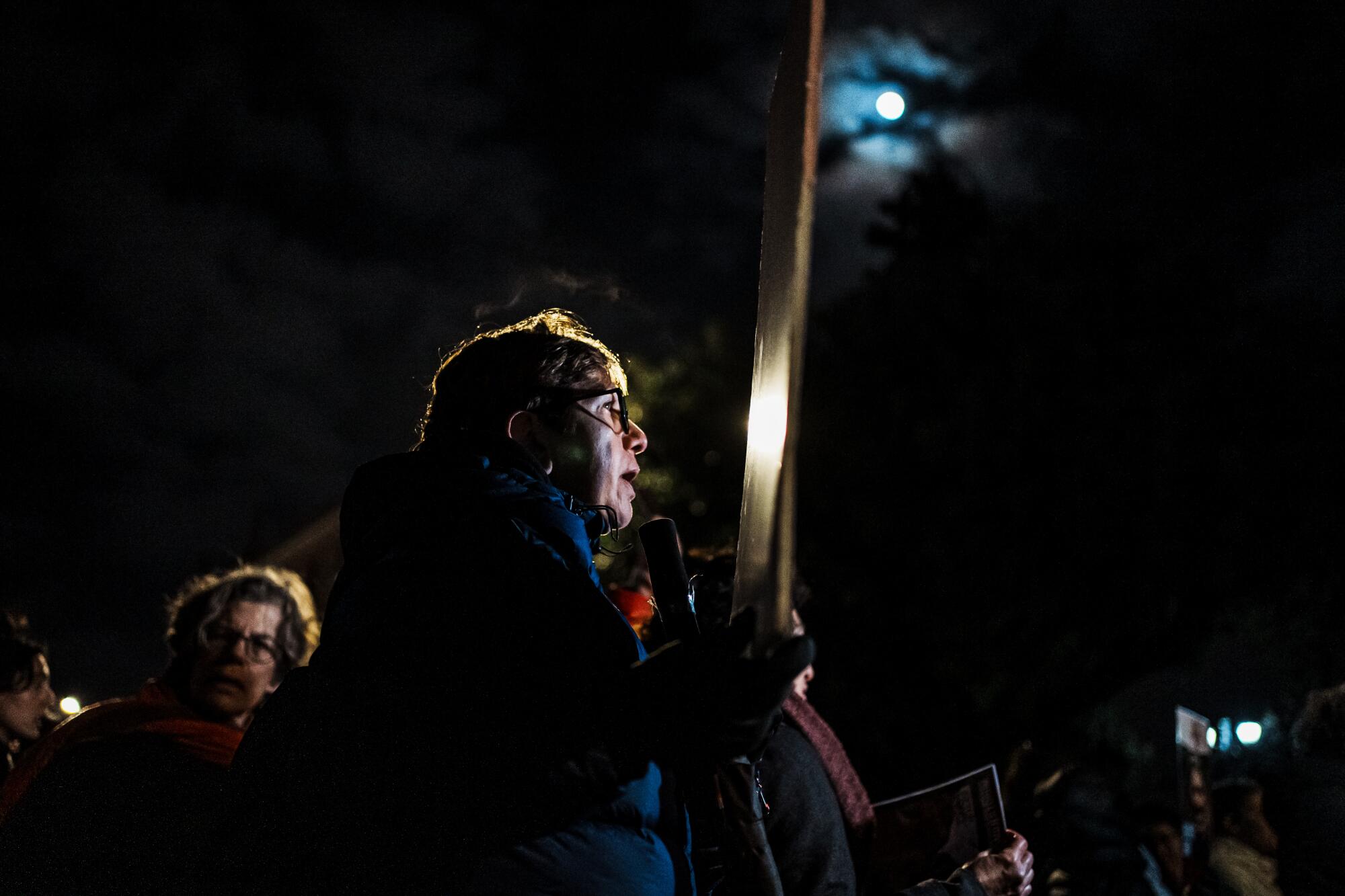 A woman joins others in protesting in the dark outside.