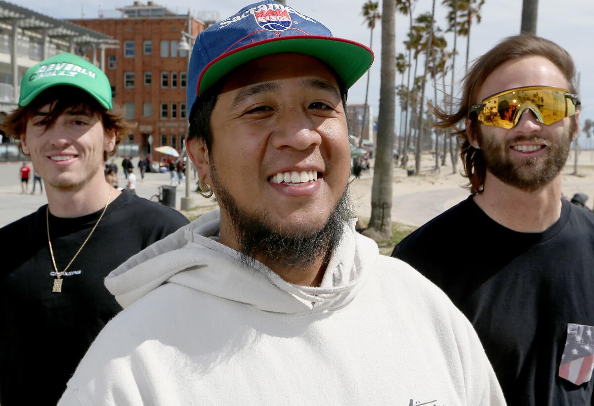 Three men pose for a portrait on the Venice boardwalk.