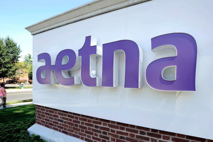 A pedestrian walks past a sign for Aetna Inc., at the company headquarters in Hartford, Conn.