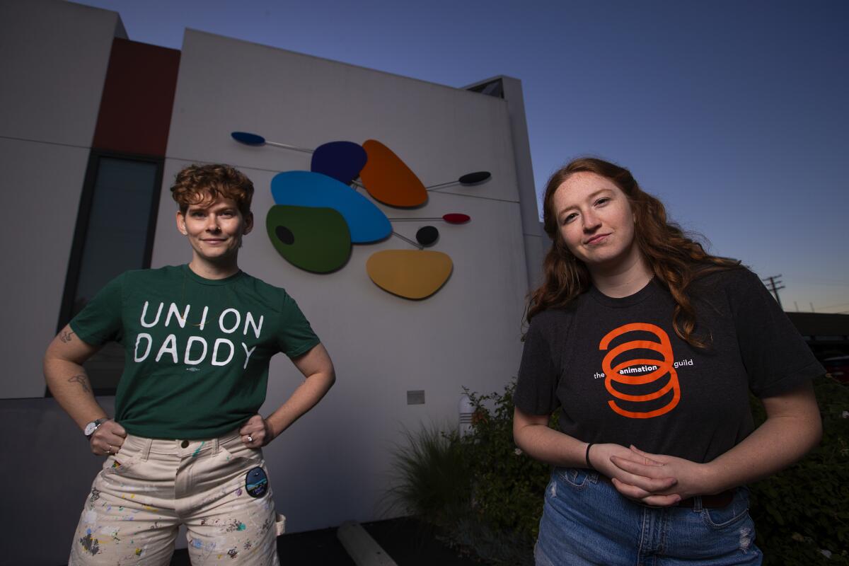 A woman wearing a green "Union Daddy" T-shirt poses in front of a building next to a woman wearing a black-and-orange T-shirt