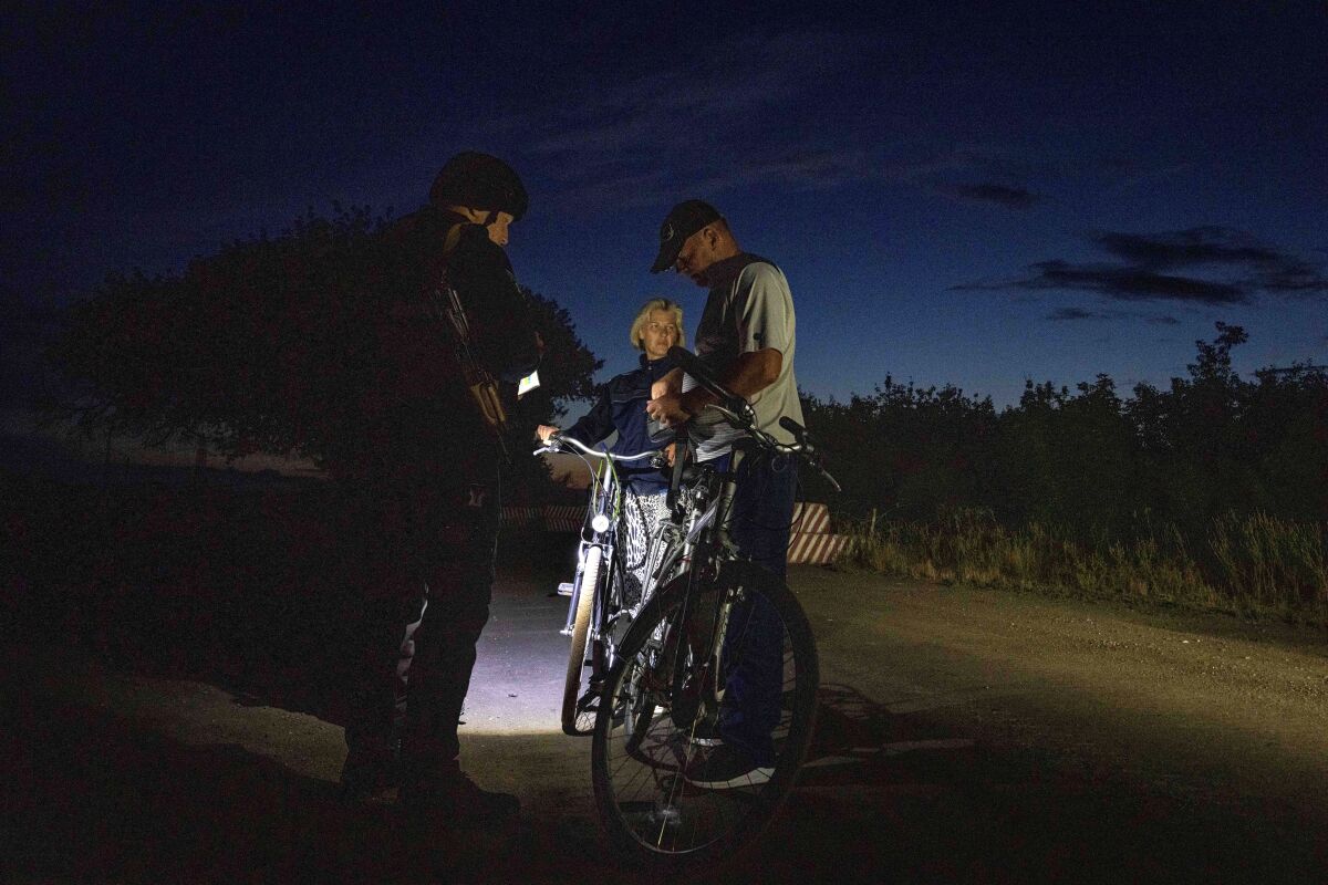 A Ukrainian police officer checks the documents of bicyclists at a checkpoint at night.