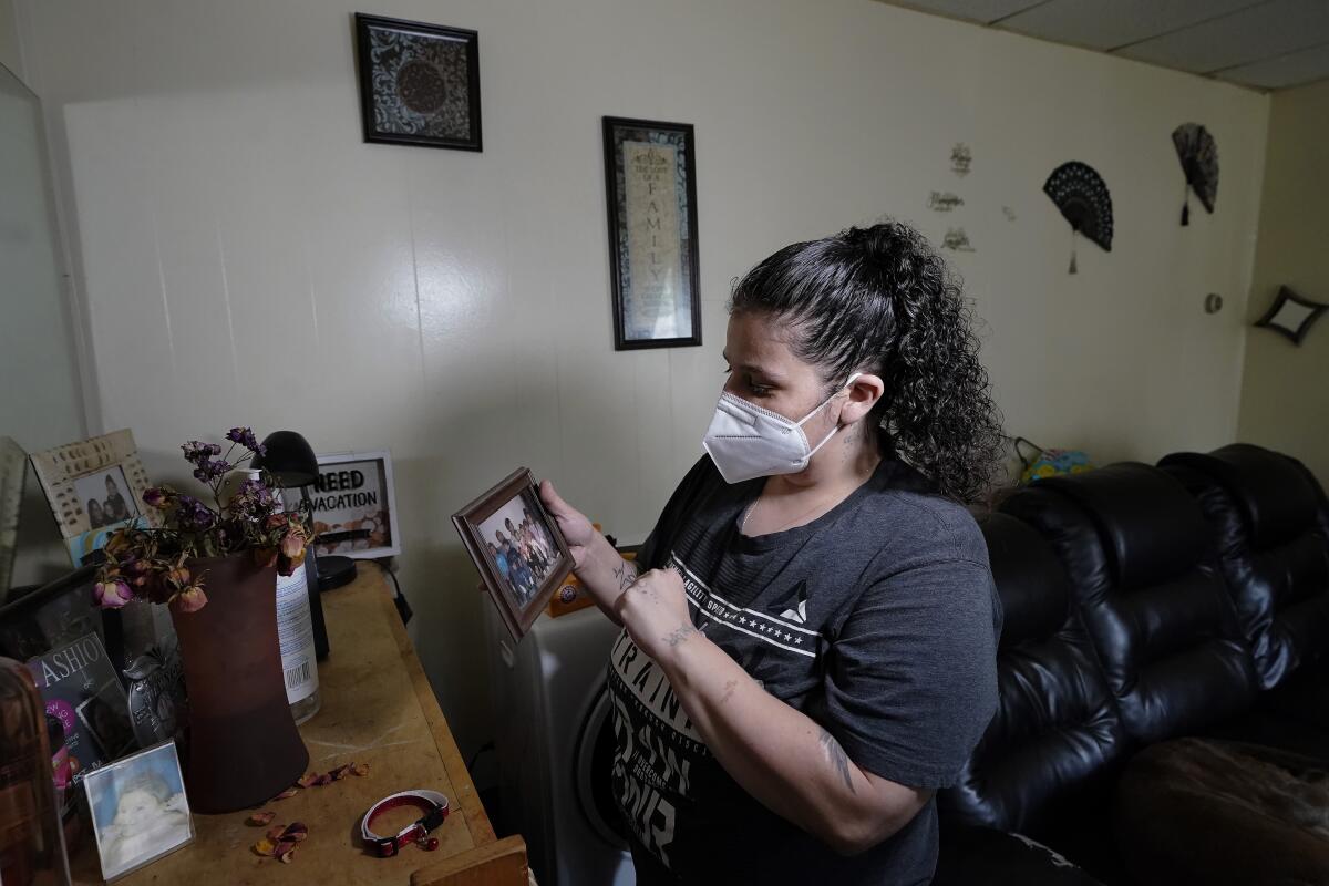 A woman in a mask holds a framed photo in her apartment.