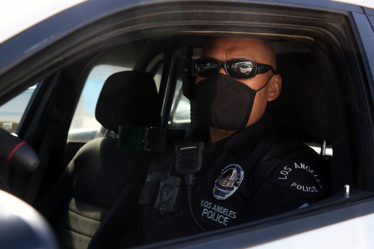 Officer Junior Nua sets out in his car wearing a black cloth mask at LAPD Harbor Station in San Pedro.  Officers have been issued two cloth masks and are required to take their temperature on entering work to make sure they are healthy.  