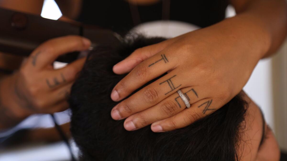 Madin Lopez, whose preferred gender pronouns 'THEY' and 'THEM' are tattooed on their hands, cuts hair in a trailer near the Los Angeles LGBTQ Youth Center in Hollywood. (Claire Hannah Collins / Los Angeles Times)