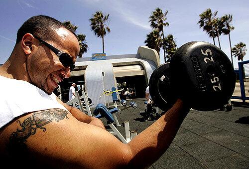 Elliot Ivey of West L.A. does preacher curls with a 25-pound dumbbell while working out at Muscle Beach.