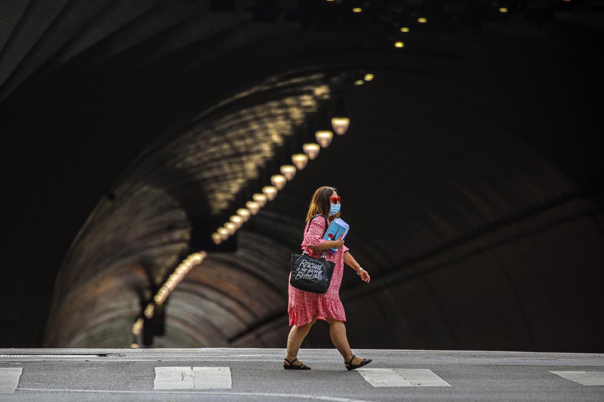A woman in a mask crosses the street in downtown Los Angeles.