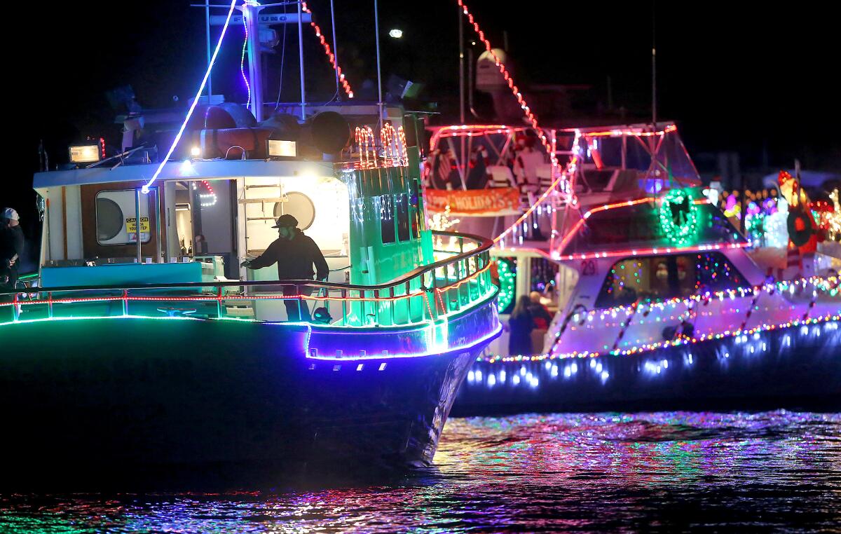 A fishing vessel and a crewman stay in line along the route during the 2019 Newport Beach Christmas Boat Parade.