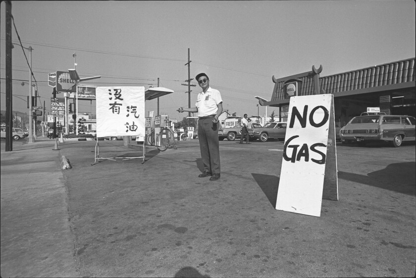 A man at a gas station points to a sign in Chinese; nearby another sign reads No gas