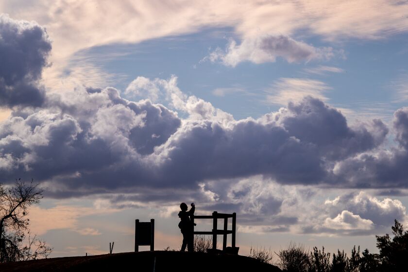Fullerton, CA - December 05: A person is silhouetted by a cloudy sky amid cool weather while taking photos of the scenic overlook of Orange and Los Angeles counties at the Panorama Nature Preserve in Fullerton Monday, Dec. 5, 2022. (Allen J. Schaben / Los Angeles Times)