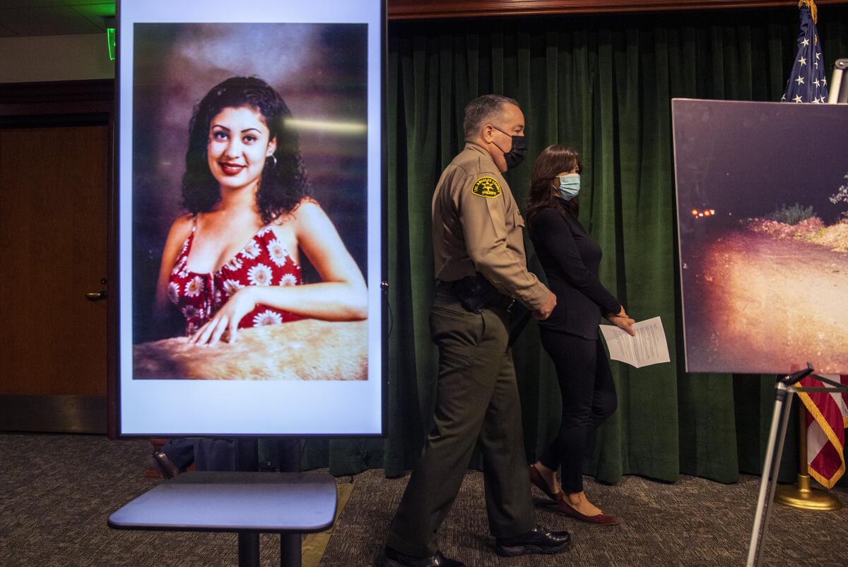 Los Angeles Sheriff Alex Villanueva and Elizabeth Arellano walk past an image of homicide victim Gladys Arellano.