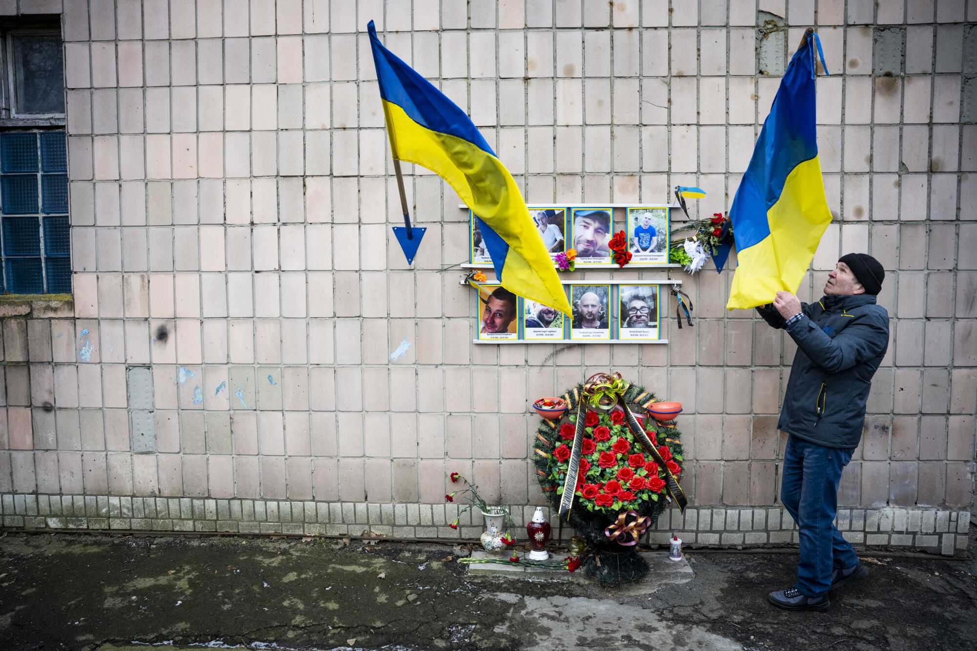 A man visiting a memorial adorned with flowers and eight portraits of victims nested between two Ukrainian flags